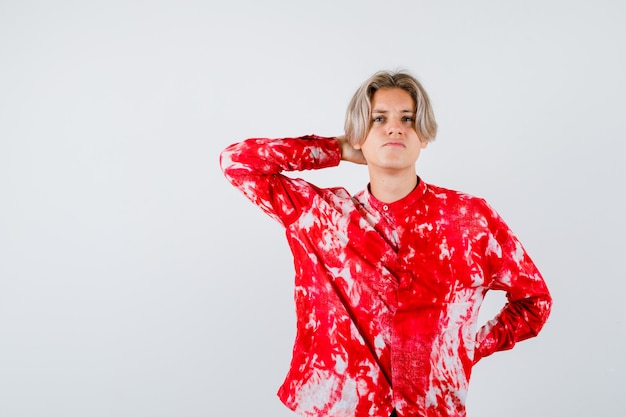 Teen blonde male in oversize shirt with hand behind head, looking up