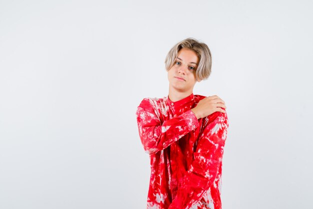 Teen blonde male in oversize shirt with hand on shoulder and looking upset , front view.