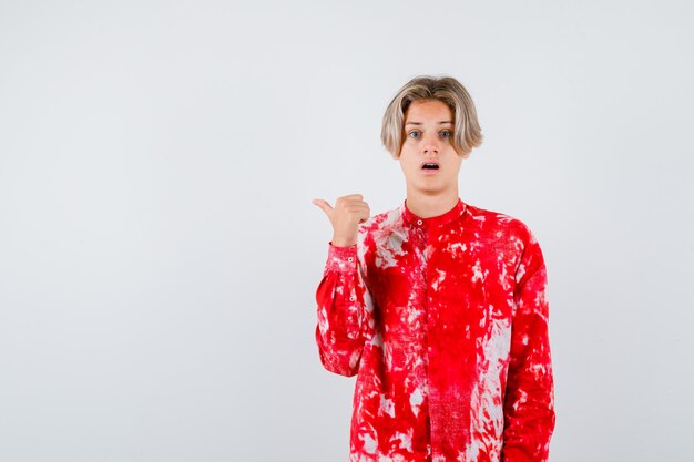 Teen blonde male in oversized shirt pointing back with thumb and looking shocked , front view.