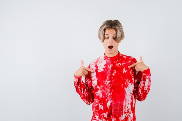 Teen blonde male in oversized shirt pointing at himself and looking shocked , front view.