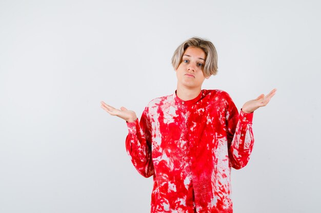 Teen blonde male showing helpless gesture in oversized shirt and looking thoughtful. front view.