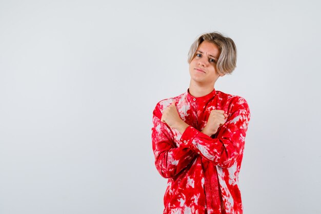 Teen blonde male showing protest gesture in oversize shirt and looking pensive , front view.