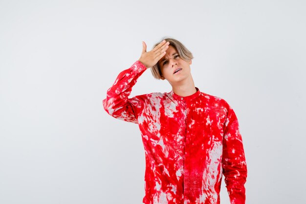 Teen blonde male with hand over forehead in oversized shirt and looking painful. front view.