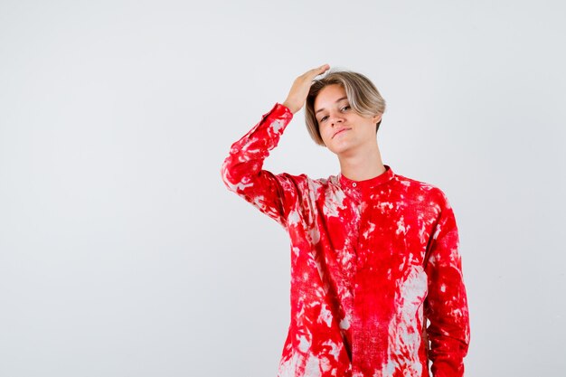 Teen blonde male with hand over head in oversized shirt and looking confident. front view.