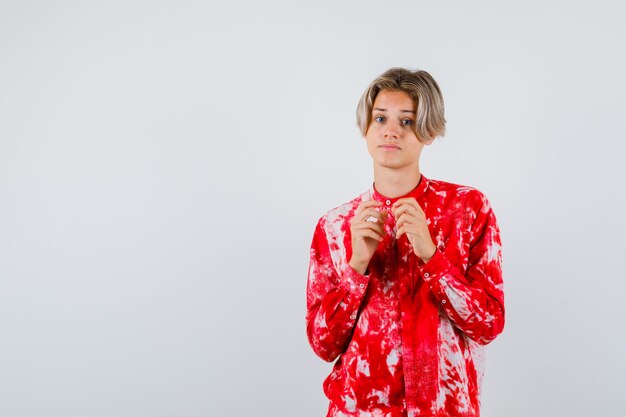 Teen blonde male with hands in front of him in oversized shirt and looking hesitant. front view.