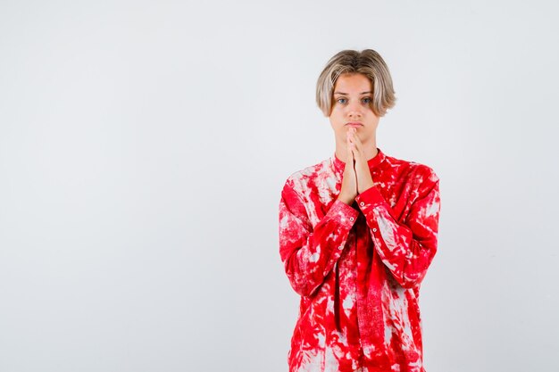 Teen blonde male with hands in praying gesture in oversized shirt and looking focused. front view.