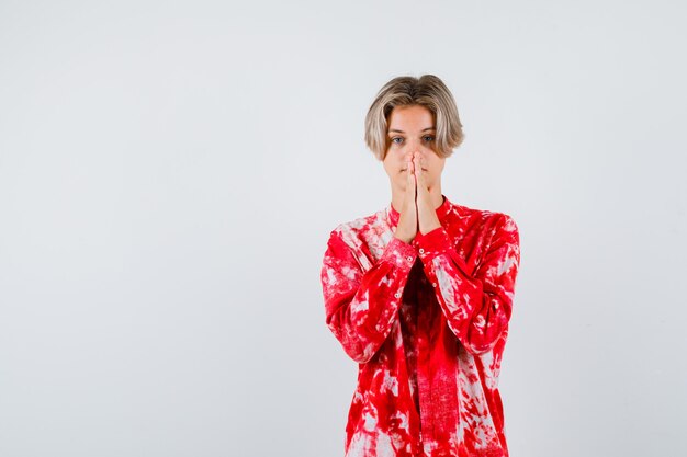 Teen blonde male with hands in praying gesture in oversized shirt and looking hopeful. front view.