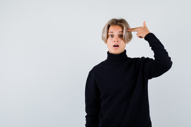 Teen boy in black sweater showing pistol hand sign and looking surprised , front view.