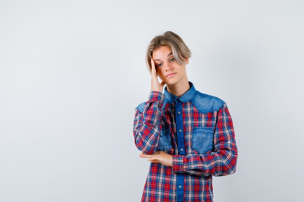 Teen boy in checkered shirt leaning head on hand and looking pensive , front view.