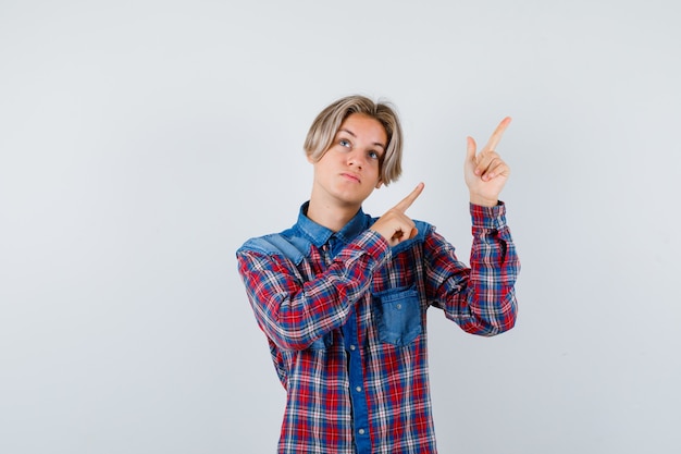 Teen boy in checkered shirt pointing aside and looking pensive , front view.