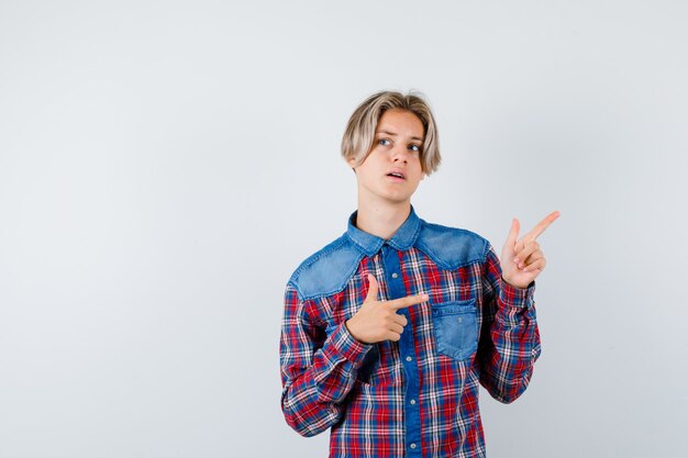 Teen boy in checkered shirt pointing aside and looking thoughtful , front view.