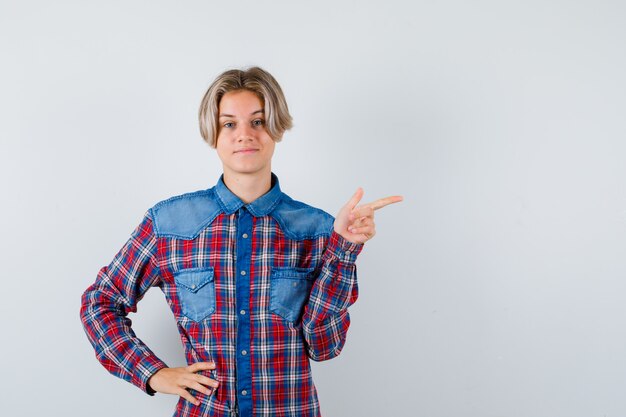 Teen boy in checkered shirt pointing to the right side and looking pleased , front view.