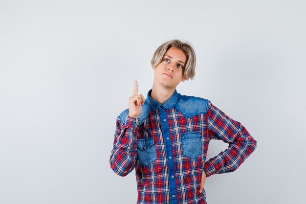 Teen boy in checkered shirt pointing up and looking pensive , front view.