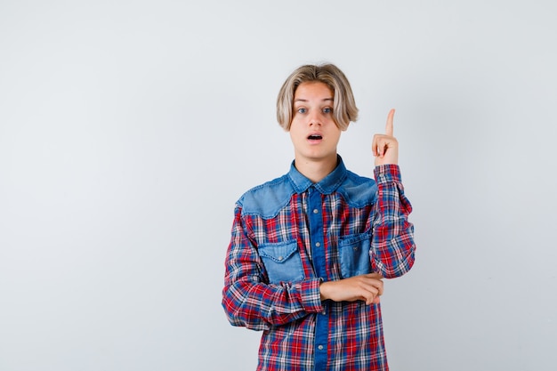 Teen boy in checkered shirt pointing up and looking perplexed , front view.