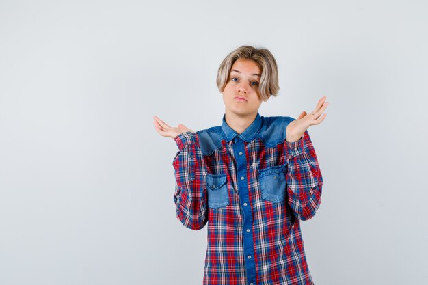 Teen boy in checkered shirt showing helpless gesture and looking indecisive , front view.