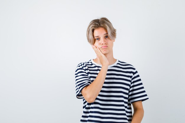 Teen boy keeping hand on cheek in t-shirt and looking preoccupied , front view.