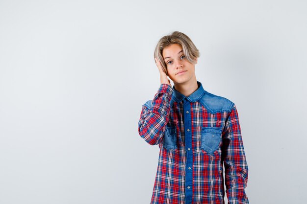 市松模様のシャツを着て頭を抱えて平和に見える10代の少年。正面図。