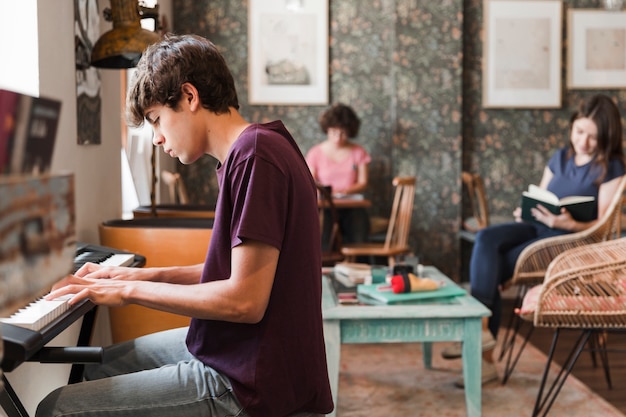 Free photo teen boy playing piano in cafe