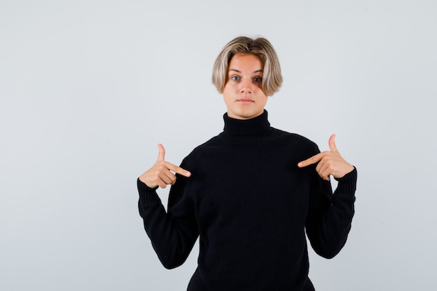 Teen boy pointing down in black sweater and looking wistful , front view.