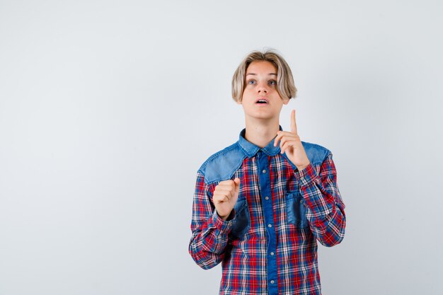 Teen boy pointing up in checkered shirt and looking perplexed. front view.