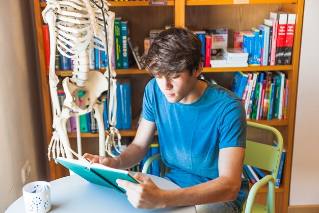 Teen boy reading book at library table