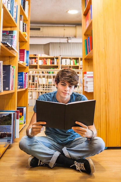 Подросток мальчик читает на пол библиотеки