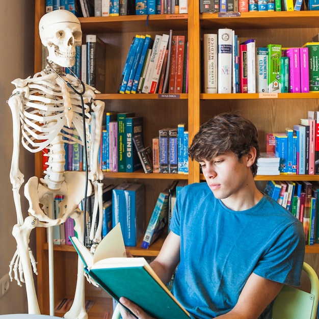 Free photo teen boy reading near skeleton