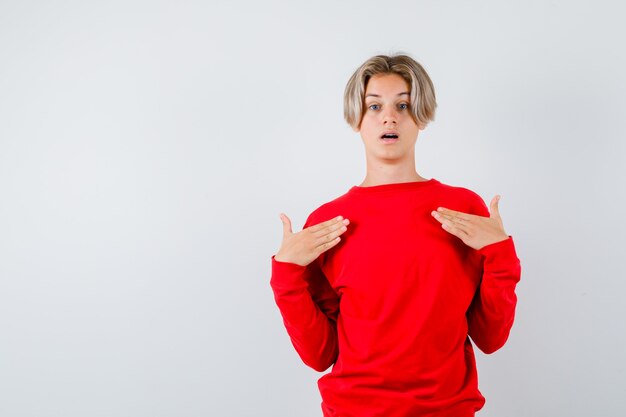 Teen boy in red sweater with hands over chest and looking astonished , front view.