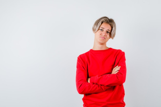 Teen boy in red sweater with hands crossed and looking displeased , front view.