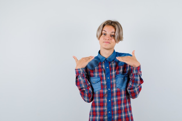 Teen boy showing height gesture in checkered shirt and looking joyful. front view.