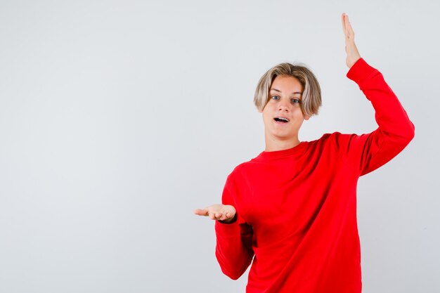 Free photo teen boy showing large size sign, opening mouth in red sweater and looking amazed , front view.