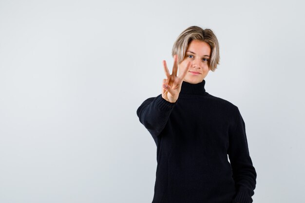 Teen boy showing three fingers in black sweater and looking cute, front view.
