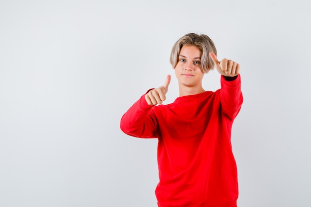 Ragazzo teenager che mostra i pollici in su in maglione rosso e sembra soddisfatto. vista frontale.