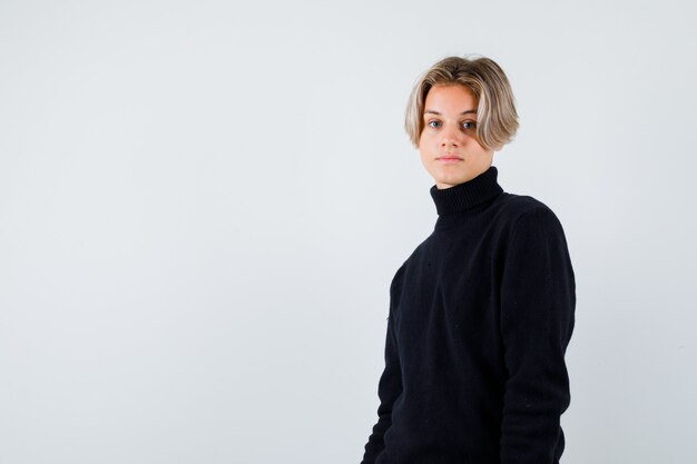 Teen boy standing sideways in black sweater and looking thoughtful.