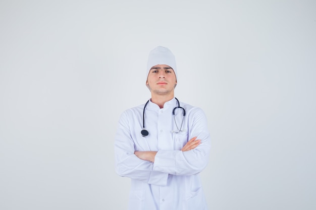 Ragazzo adolescente in piedi con le braccia incrociate in uniforme medico e guardando fiducioso