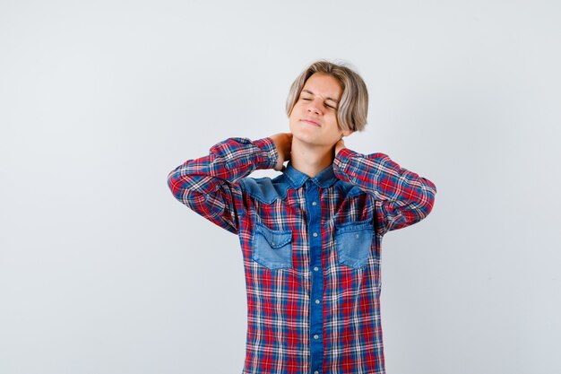 Teen boy suffering from neckache in checkered shirt and looking painful. front view.