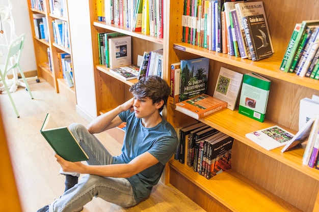 Ragazzo teenager che sostiene testa e che legge sul pavimento