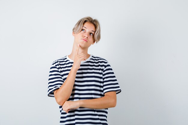 Teen boy in t-shirt keeping finger on chin and looking pensive , front view.