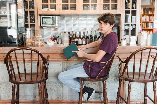 Free photo teen boy with book near vintage counter in cafe