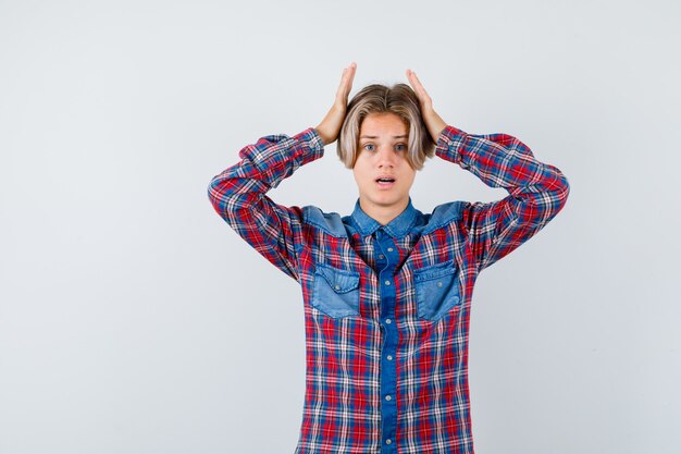 Teen boy with hands on head in checkered shirt and looking forgetful , front view.