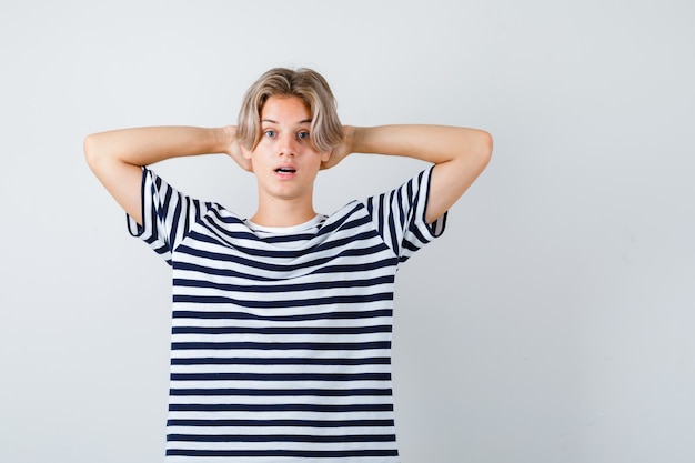 Teen boy with hands behind head, opening mouth in t-shirt and looking surprised. front view.