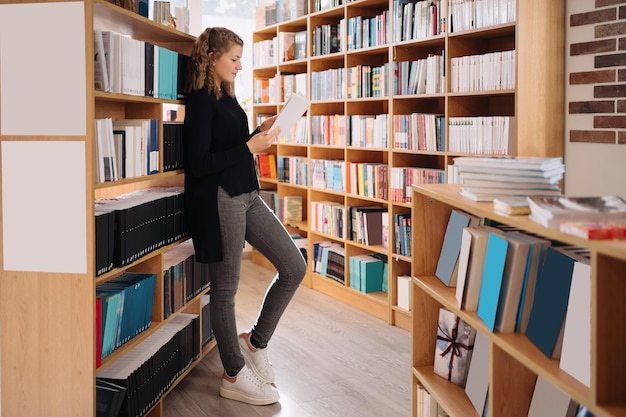 Free photo teen girl among a pile of books. a young girl reads a book with shelves in the background. she is surrounded by stacks of books. book day.