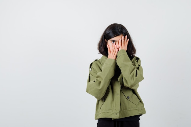 Teen girl in army green jacket holding hands on face and looking subdued , front view.