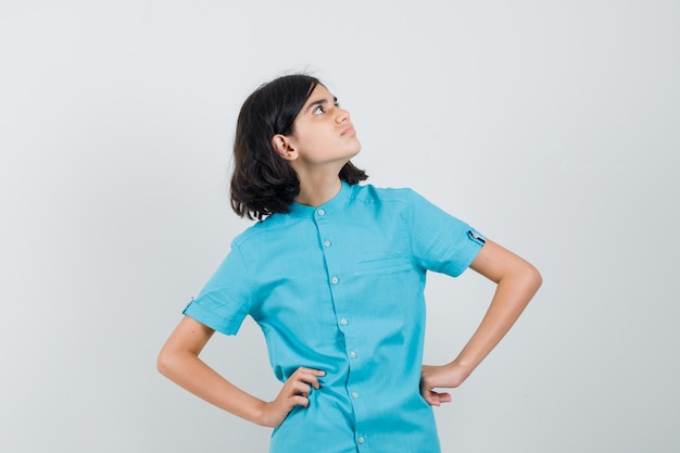 Teen girl in blue shirt looking upper left corner with hands on waist and looking focused