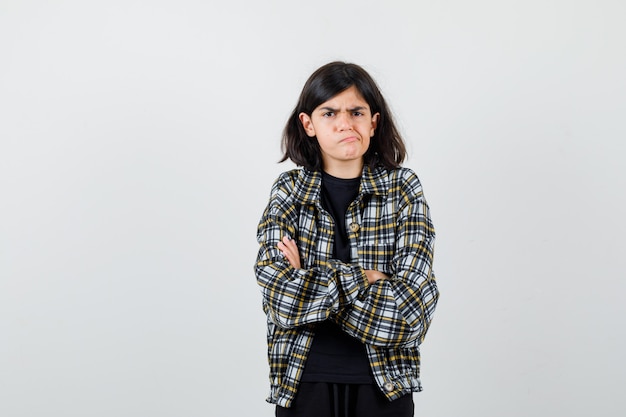 Teen girl in casual shirt holding arms folded, curving lower lip and looking grumpy , front view.