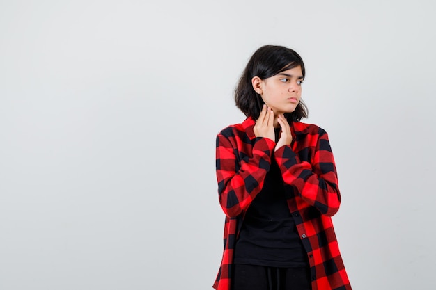 Teen girl in casual shirt holding hands under chin, looking aside and looking bewildered , front view.