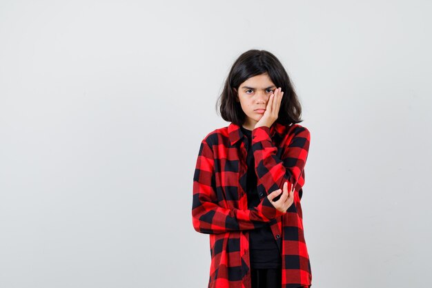 Teen girl in casual shirt leaning cheek on palm and looking upset , front view.