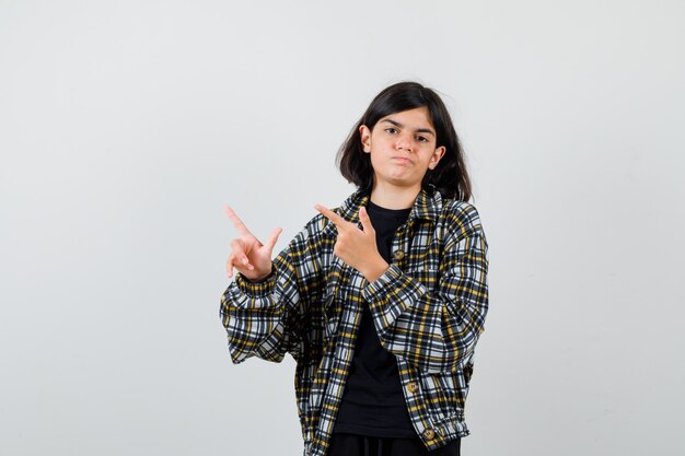 Teen girl in casual shirt pointing at upper left corner and looking disappointed , front view.