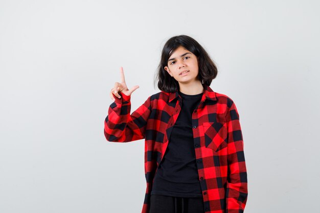 Teen girl in casual shirt showing loser gesture and looking cheerless , front view.