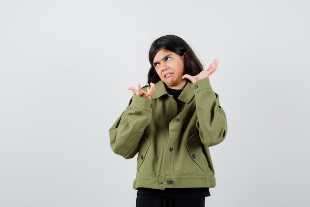 Teen girl doubting while shrugging shoulders in t-shirt, jacket and looking focused , front view.